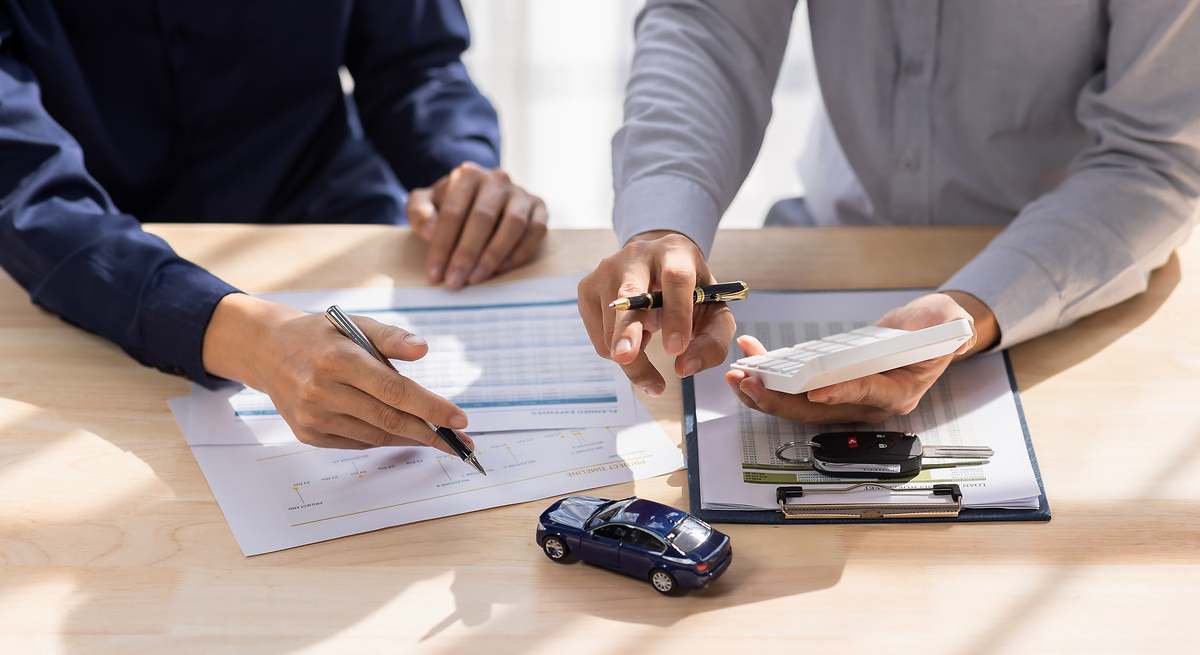 Profesionales revisando documentos y calculadora para determinar el valor asegurado de un auto.
