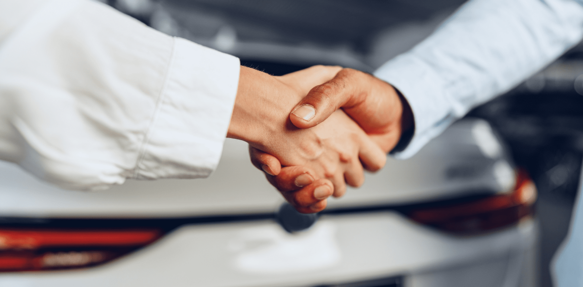 Dos personas estrechando la mano frente a un vehículo, evaluando si están pagando caro el seguro en una negociación empresarial.