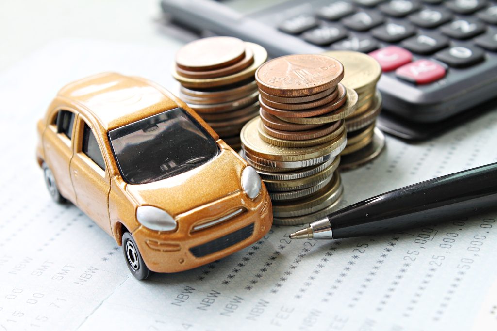Auto en miniatura junto a monedas y calculadora, ilustrando el análisis para determinar si una empresa está pagando caro el seguro automotor.