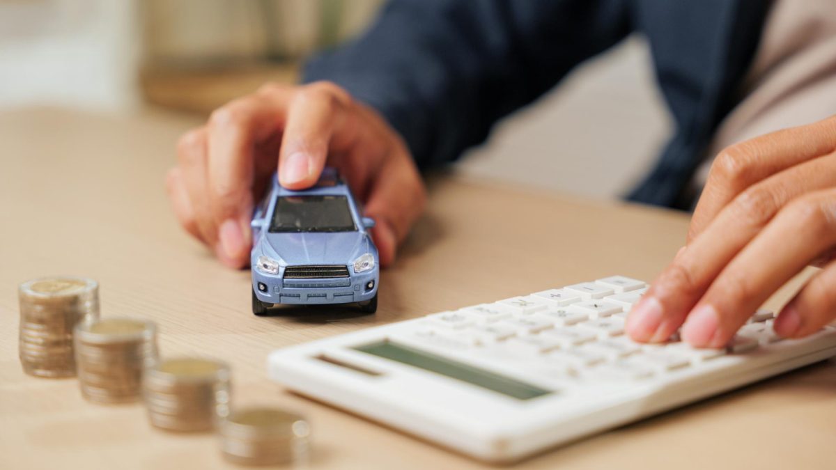 Persona utilizando calculadora junto a un auto en miniatura y monedas para estimar el costo de la Transferencia del auto.