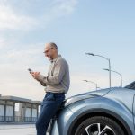 Conductor utilizando su teléfono móvil junto a su vehículo para comparar seguros de auto en Uruguay de forma digital.