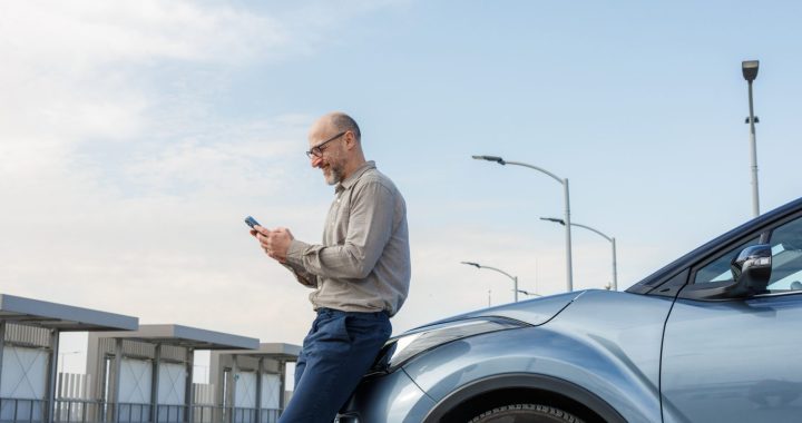 Conductor utilizando su teléfono móvil junto a su vehículo para comparar seguros de auto en Uruguay de forma digital.