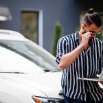 Profesional analizando información en laptop junto a su vehículo para verificar el valor asegurado.